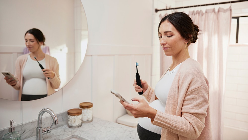 A pregnant woman checking her brushing behaviors on an app, while holding a toothbrush in her other hand